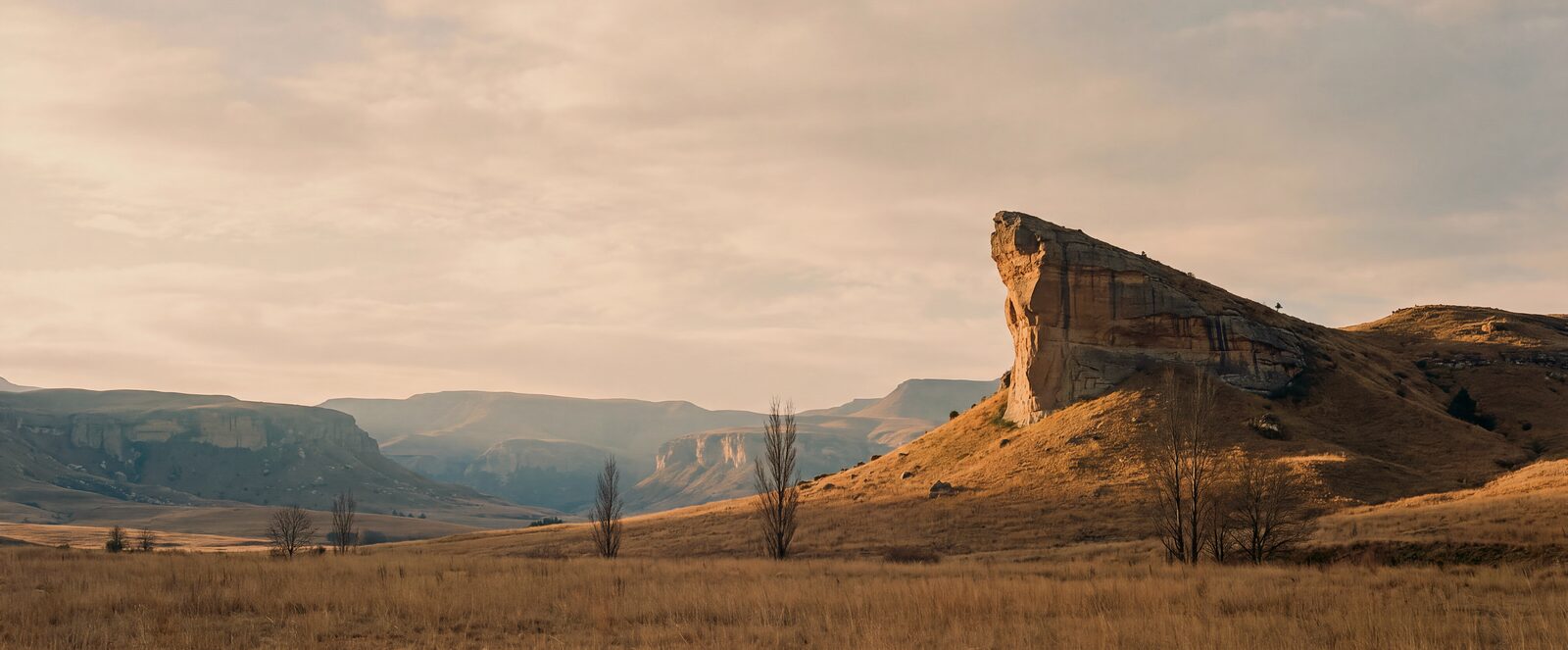 Titanic Rock, the ship-prow sandstone landmark north of Clarens, catching low golden light with the Maluti escarpments beyond